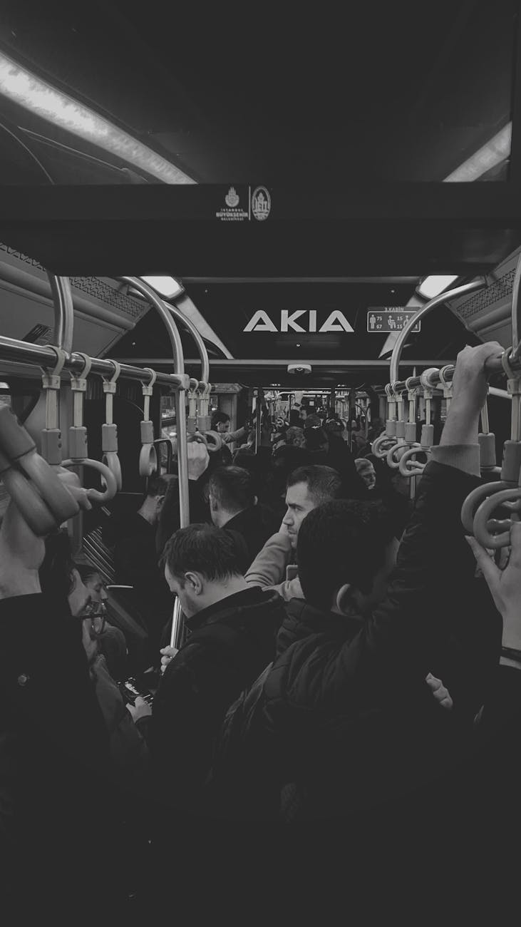 Ayakta duran yolcuların bulunduğu kalabalık bir otobüsün içini gösteren siyah beyaz fotoğraf.
