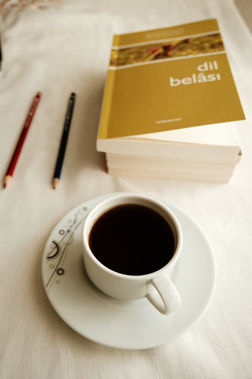Masada kahve, kitaplar ve kalemlerin bulunduğu, sıcak ve davetkar bir okuma ortamı.