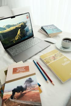 Aydınlık bir masa üzerinde dizüstü bilgisayar, kitaplar, kahve ve kırtasiye malzemeleri bulunan, sakinleştirici bir çalışma alanı.