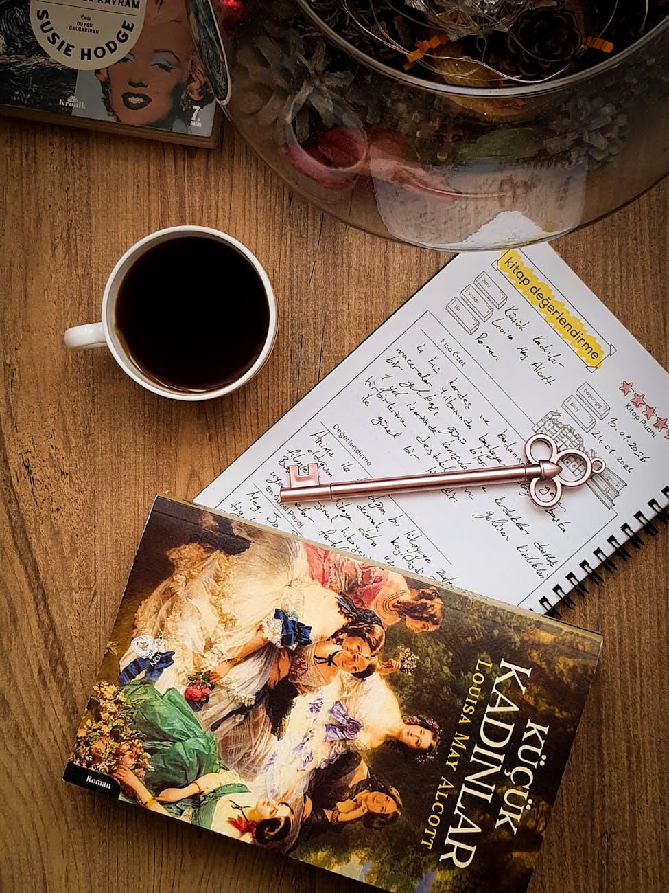 Kitap, defter, kahve ve dekoratif bir anahtarın yer aldığı, samimi bir düz yerleşim fotoğrafı.