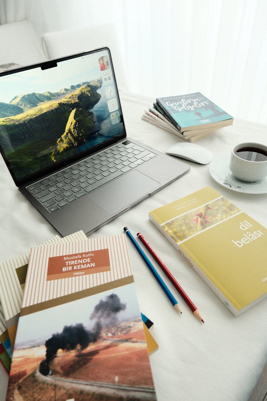 Aydınlık bir masa üzerinde dizüstü bilgisayar, kitaplar, kahve ve kırtasiye malzemeleri bulunan, sakinleştirici bir çalışma alanı.