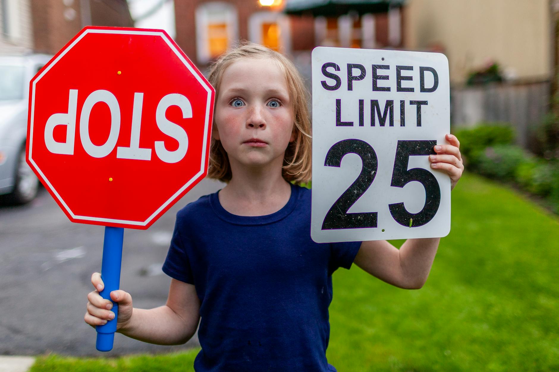 Yerleşim bölgesinde ters takılmış dur levhası ve hız sınırı levhası gören şaşırmış bir kız.